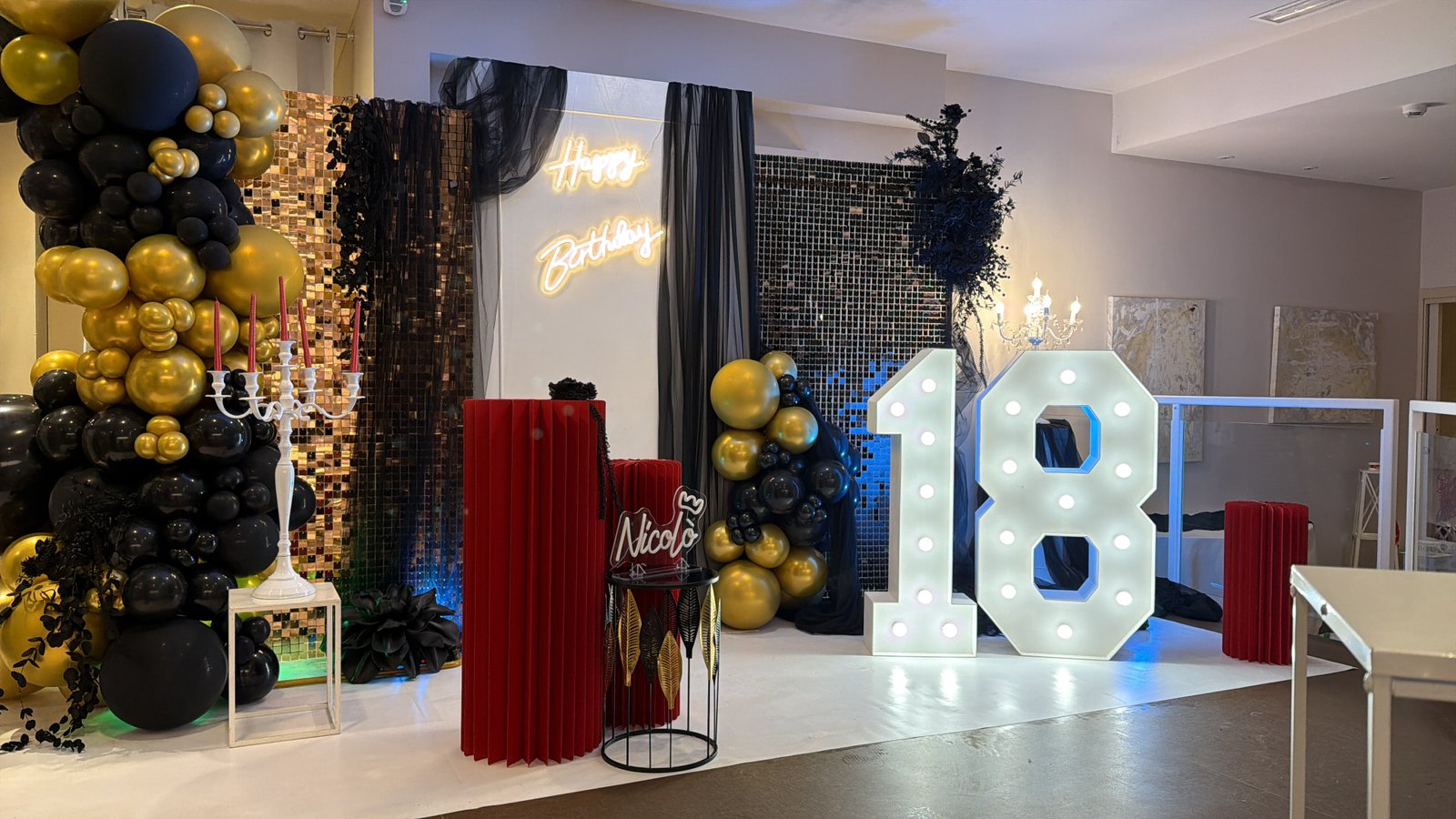 18esimo compleanno elaborato con palloncini neri e oro, drappeggi, candelabro e numeri luminosi 18