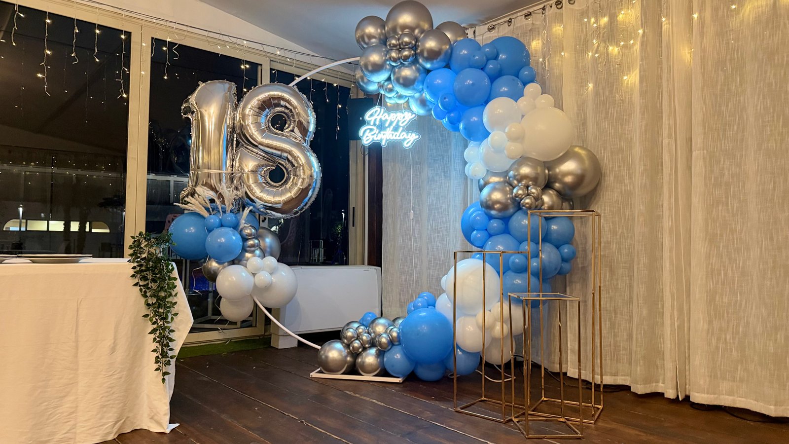 18esimo compleanno con arco palloncini blu, argento e bianchi, numeri foil 18 e stand dorati